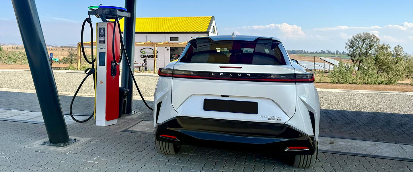 Rear view of a white Lexus RZ beside a solar-powered Charge station