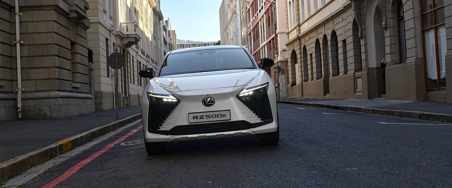 White Lexus RZ driving along a narrow city street