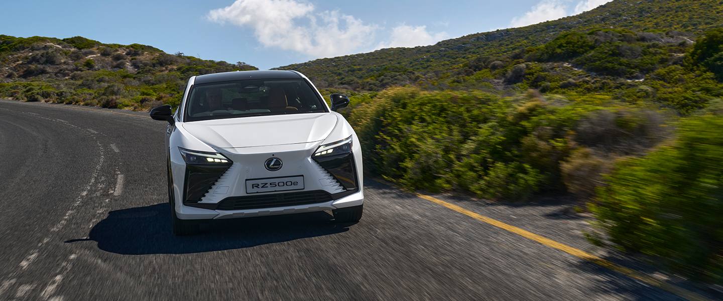 White Lexus RZ driving through a green mountain landscape