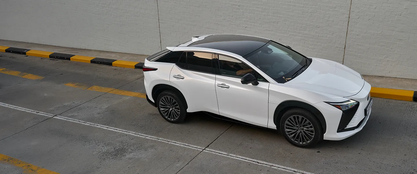 The white Lexus RZ driving along a tree-lined road